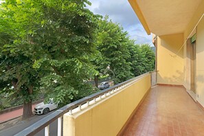 Un balcon doté d’un sol carrelé, d’une balustrade et offrant une vue sur une rue bordée d’arbres.