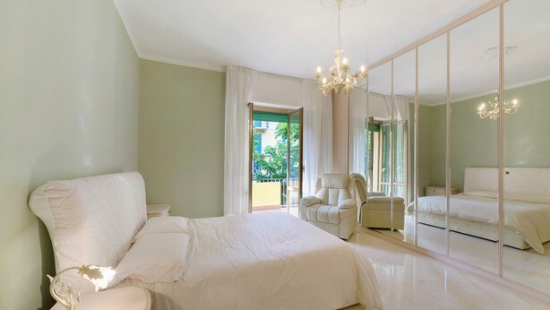 A bedroom with a large bed, a chair, a nightstand, a mirror, and a chandelier. - Apartment 'Casa Nonna Adri' with Shared Terrace and Wi-Fi (levanto)