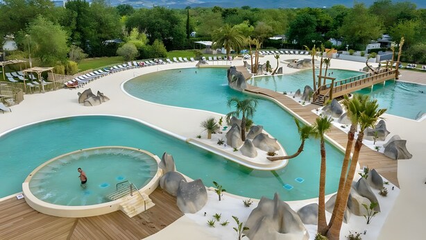 A resort pool with multiple sections, palm trees, and a mountainous backdrop. - Mobile Home Caravan with Shared Pool and Private Terrace (Unknown)