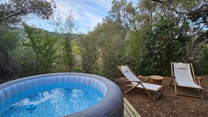 An outdoor hot tub surrounded by trees, with two wooden lounge chairs. - Samadhi Holiday Home with Mountain Views, Wi-Fi, and Air Conditioning (Toulon)