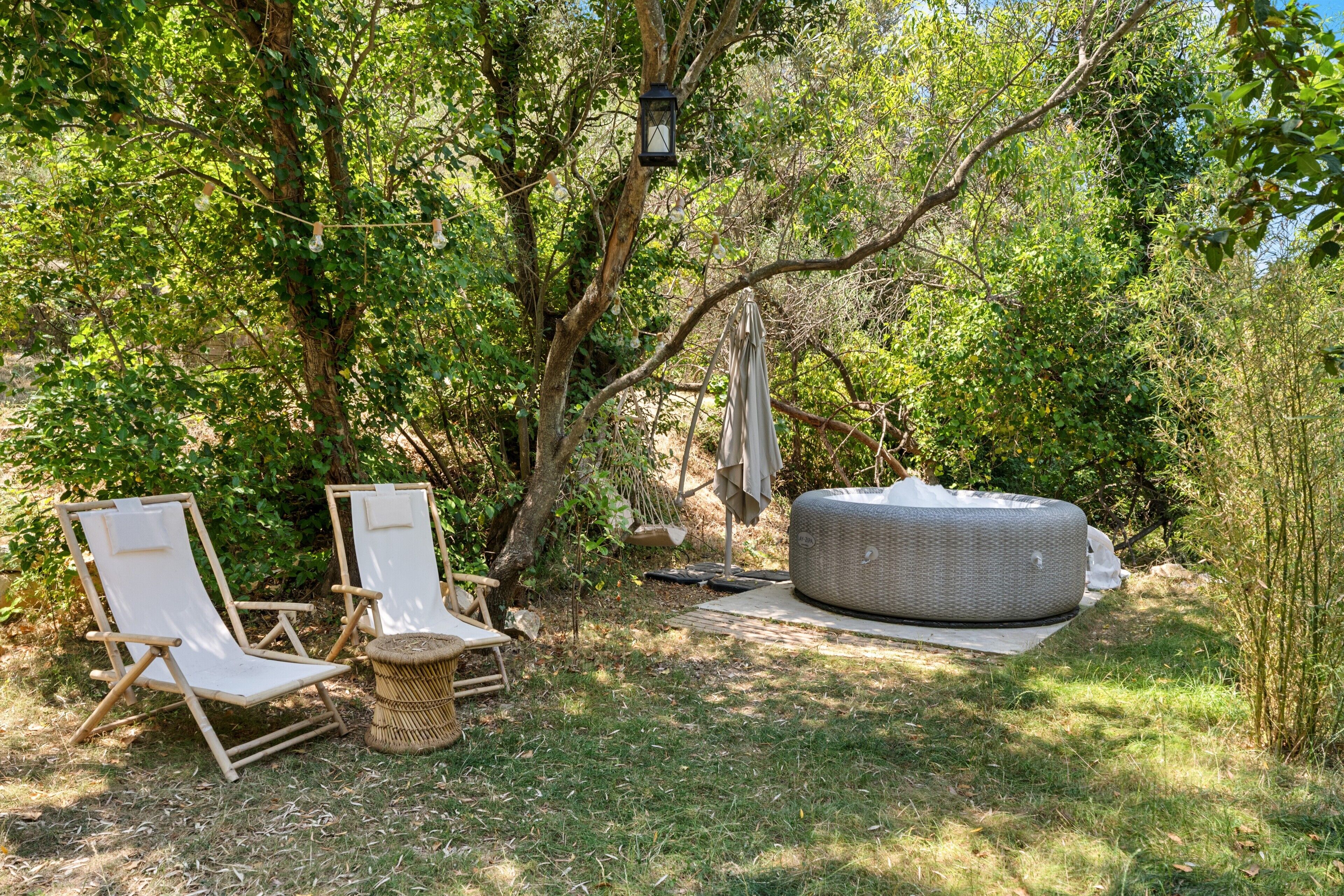 Een tuin met twee witte lounge fauteuils, een rieten poef en een hanglamp.