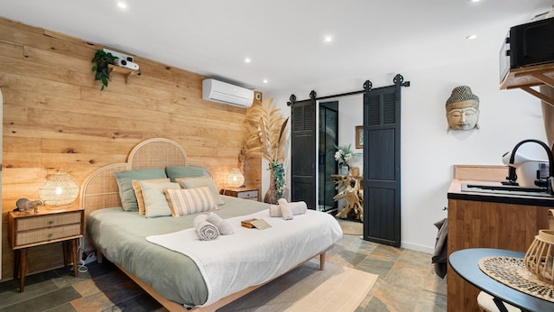 A bedroom with a wooden headboard, a bed with a white comforter, a bedside table with a lamp, and a wall-mounted air conditioner. - Samadhi Holiday Home with Mountain Views, Wi-Fi, and Air Conditioning (Toulon)