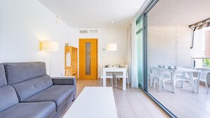 A modern living room with a grey sofa, a white coffee table, and a dining area with white chairs and a table.