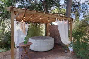 A wooden pergola with string lights, a round bean bag chair, and a small table with a bottle.