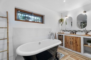 A modern bathroom with a freestanding bathtub, wooden cabinets, and a window with a view of trees.