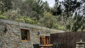 Un jacuzzi rodeado por un muro de piedra, una mesa de madera con sillas y un patio con césped.