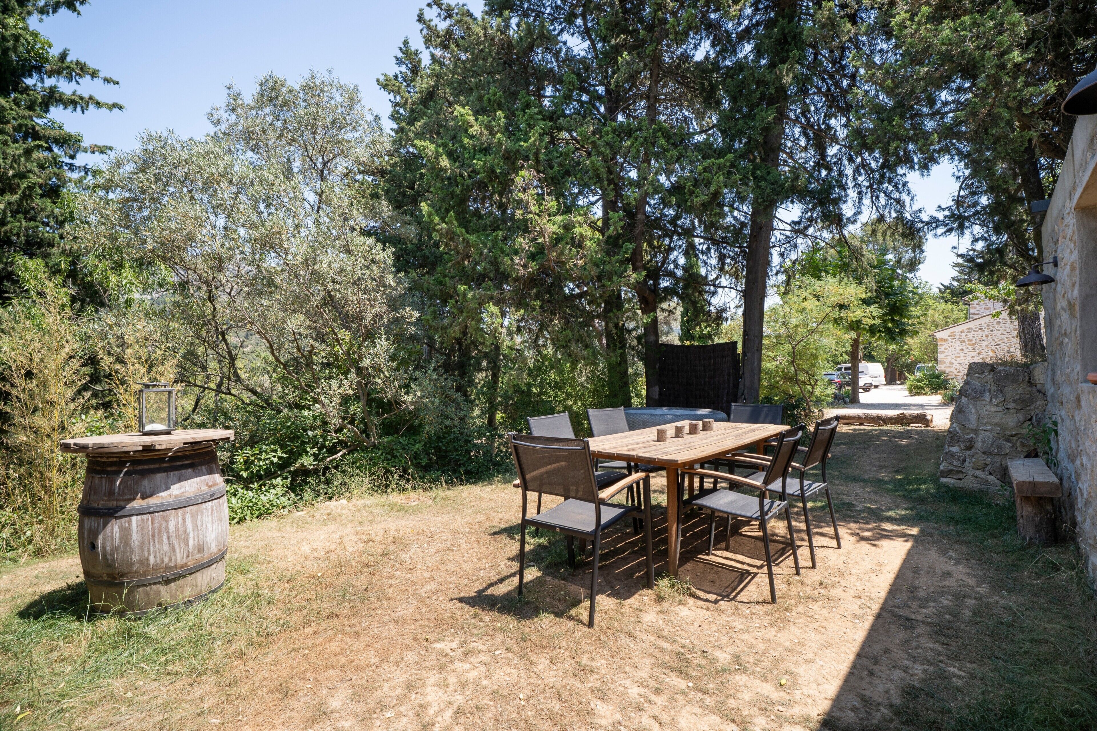 Un'area pranzo all'aperto con tavolo e sedie in legno, circondata da alberi e un muro di pietra.