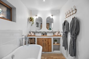 A modern bathroom with a bathtub, wooden vanity, two mirrors, and a robe rack.