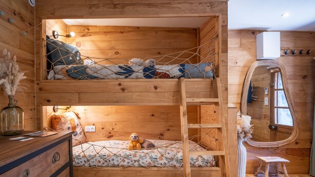 Una cama litera con escalera, un aparador, un espejo y un taburete pequeño en una habitación de madera.