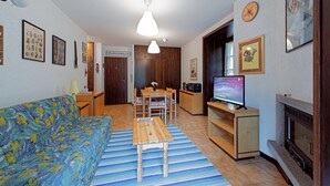 Een woonkamer met een bank, een salontafel, een televisie, een open haard en een eethoek met stoelen en een tafel.