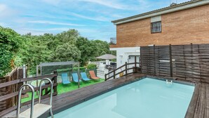 A swimming pool with a wooden deck, a brick building, and a fenced area with slides.