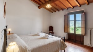 Een slaapkamer met een bed, een stoel, een raam met uitzicht en een houten plafond.