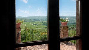 Uitzicht door een raam met balkon, op een landschap met glooiende heuvels en een heldere lucht.