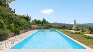 A rectangular swimming pool with a stone border, surrounded by a grassy area and a stone wall.