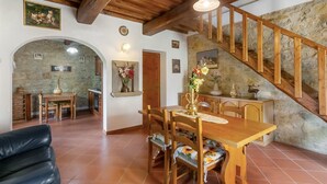 A dining area with a wooden table and chairs, a staircase with wooden railings, and stone walls. - Apartment 'Il Magnifico' with Shared Pool, Private Terrace and Wi-Fi (Unknown)
