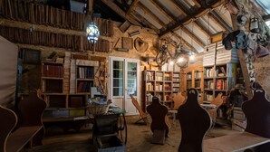 Une pièce au décor rustique, avec des étagères en bois remplies de livres, un vélo d’époque et une collection de chapeaux et de casques.