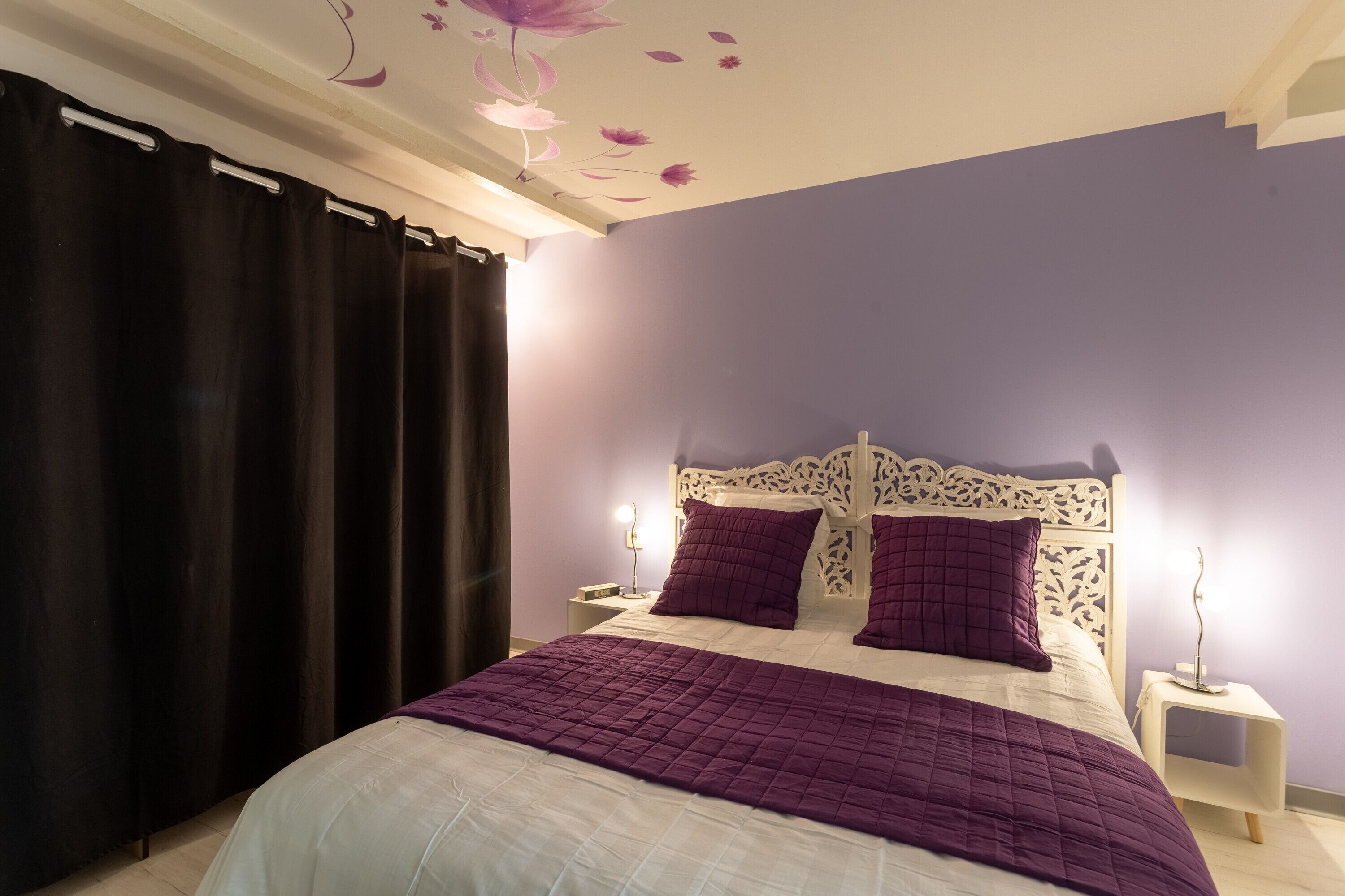 Ein Schlafzimmer mit einem Bett, Vorhängen, einem Nachttisch und einer Wand mit Blumenstickern.