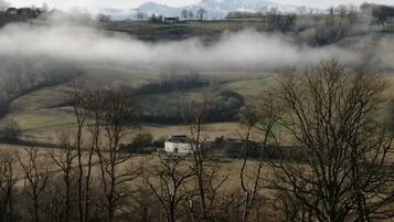 Un paysage rural avec des collines ondoyantes, un bâtiment blanc et une chaîne de montagnes à l’horizon.