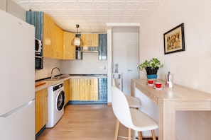 A compact kitchen with wooden cabinets, a washing machine, a sink, and a bar area with stools.