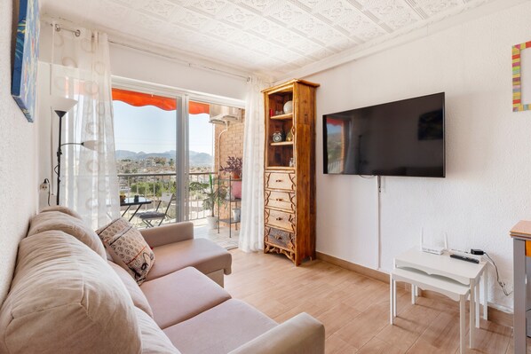 A living room with a sofa, a TV, a wooden cabinet, and a balcony with a view. - Apartment 'Vistas Al Mar' with Sea View, Wi-Fi and Air Conditioning (Unknown)