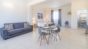 Un salon moderne comprenant un canapé, une table à manger, des chaises, un lit et une salle de bain visible à travers une porte ouverte.