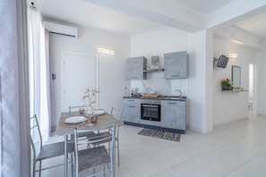Una cocina moderna con armarios grises, horno empotrado y zona de comedor con mesa y sillas.