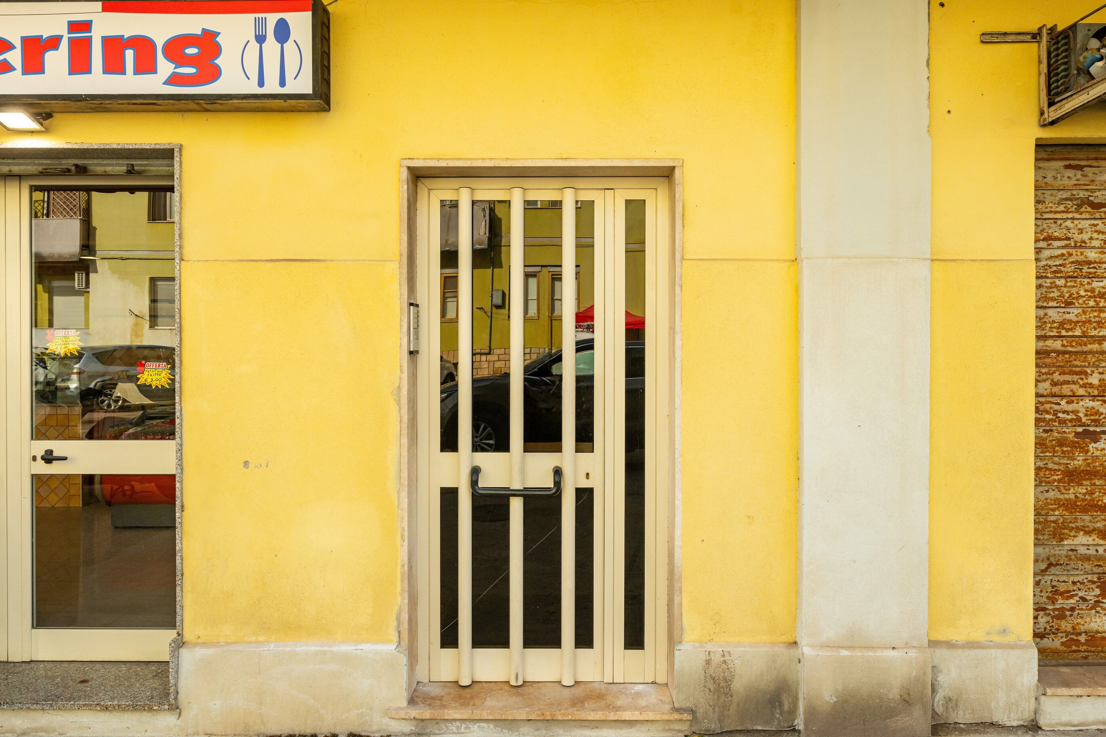 Un bâtiment jaune avec une enseigne sur laquelle on peut lire le mot « sonner » et une porte dotée d’un portail en métal.