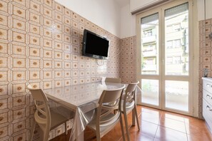 Ein Essbereich mit einer Fliesenwand, einem an der Wand montierten Flachbildfernseher über einem Tisch und einer Glasschiebetür, die auf einen Außenbalkon führt.