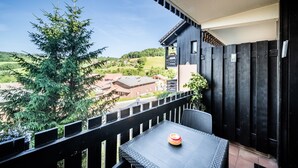 Un balcón con mesa y sillas, vista a un árbol y un edificio al fondo.