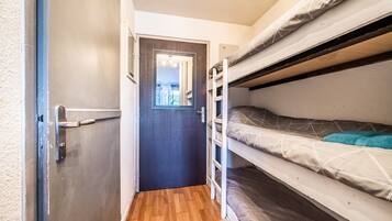 Une petite pièce avec un lit superposé, une porte dotée d’un miroir et un plancher en bois.