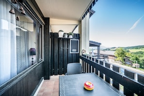 En balkon med et bord, stole, en potteplante og udsigt til en bro og et landskab.