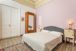 Un dormitorio con cama, mesitas de noche, cómoda, espejo y suelo estampado.