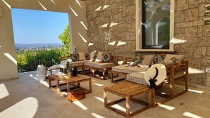 A sunlit patio with a stone wall, a large window, and a view of greenery.