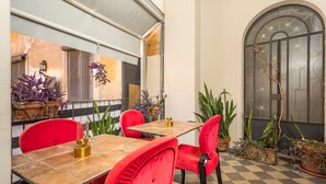 A dining area with a checkered floor, red chairs, a table with a gold centerpiece, and potted plants.