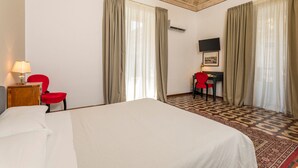 A hotel room with a large bed, a desk, a chair, a TV, and a patterned carpet.