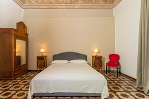 Ein Hotelzimmer mit einem großen Bett, zwei Nachttischen mit Lampen, einem roten Sessel und einem Holzschrank.