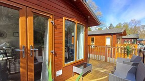 Une cabane en bois dotée de grandes portes-fenêtres coulissantes, d’une terrasse avec des meubles en osier et d’un petit espace salon extérieur.