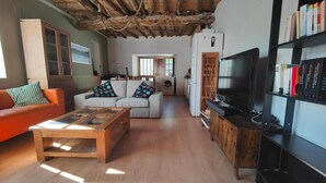Una sala de estar con sofá, mesa de centro, televisor, estantería y un área de cocina con lavadora.