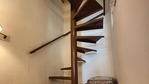 Una escalera de caracol con peldaños de madera y barandillas metálicas, que conduce a un piso superior.