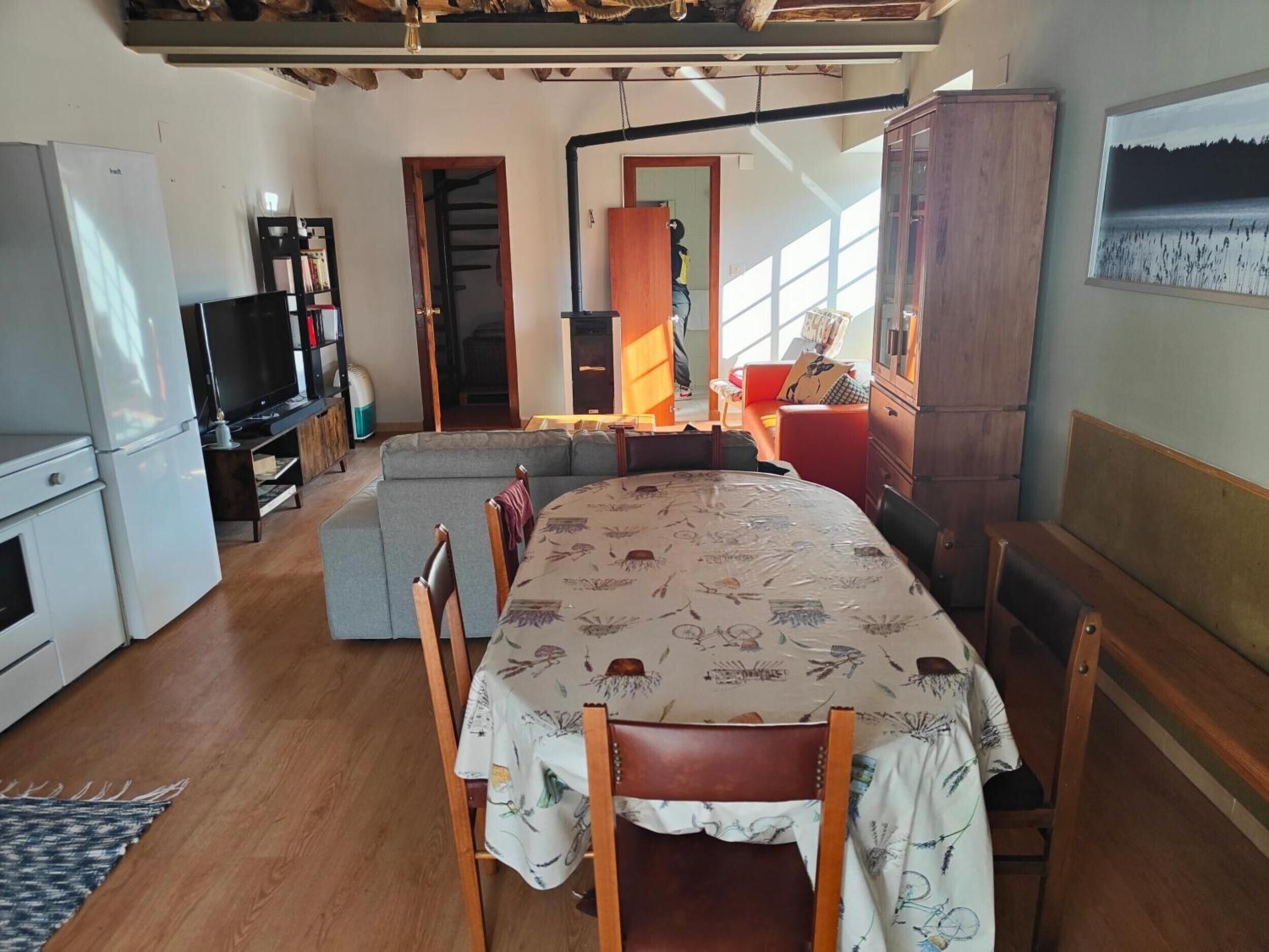 Una habitación acogedora con una mesa de comedor, sillas, un sofá, un televisor, un refrigerador y un armario.