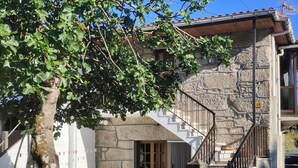 Un edificio de piedra con una escalera que conduce a una puerta de madera, un árbol en primer plano y un cielo azul despejado.