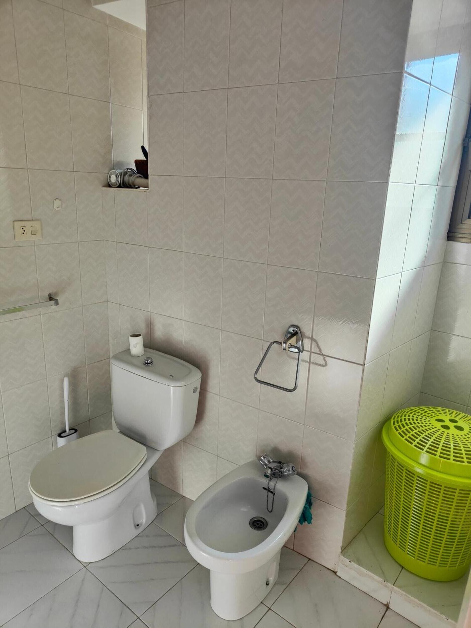 A bathroom with a toilet, bidet, and a green laundry basket.