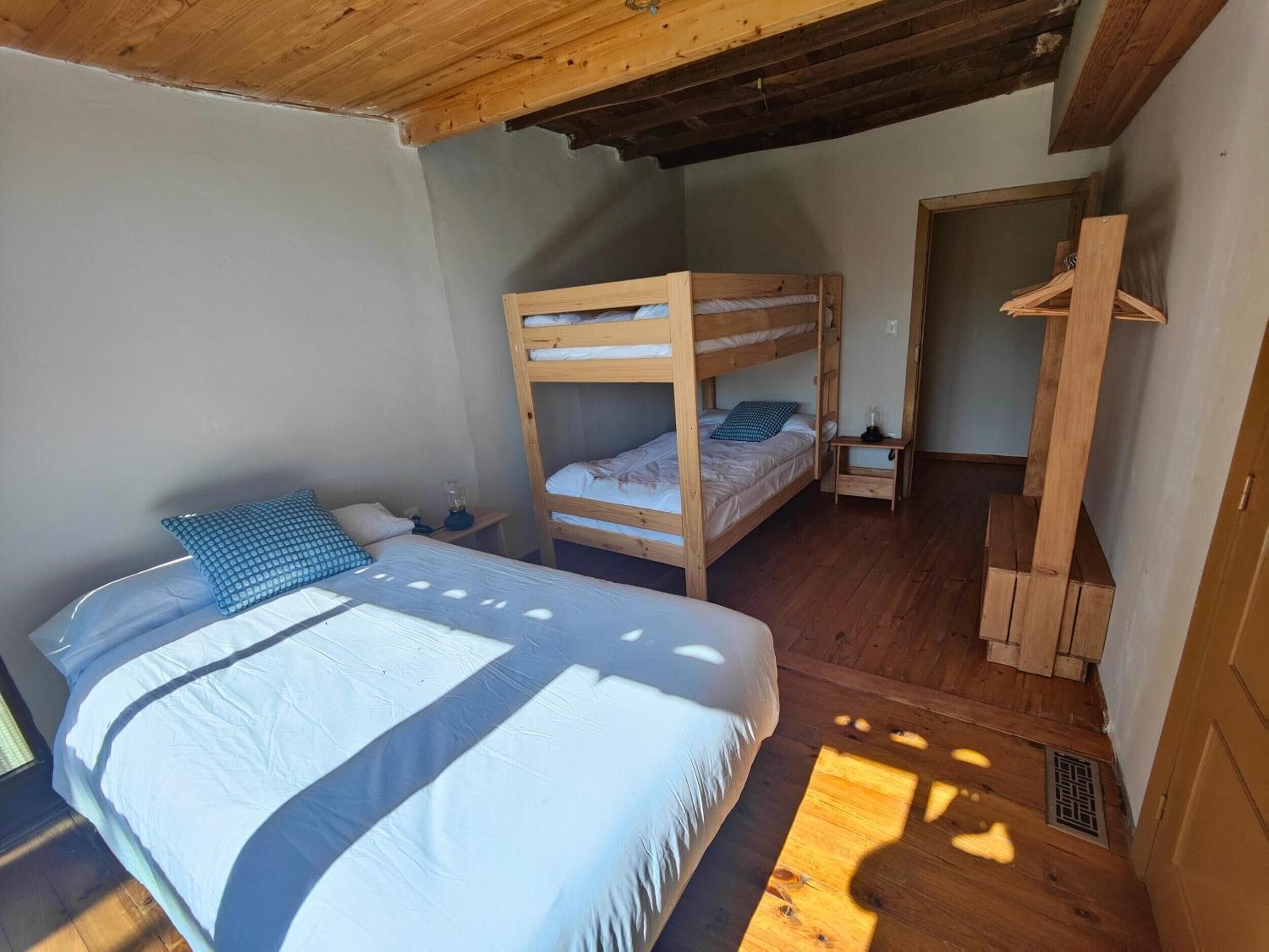 Ein Zimmer mit einem Etagenbett, einem Einzelbett, einem Holzschrank und einem kleinen Tisch mit Lampe.
