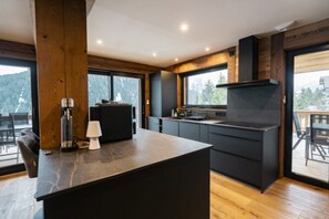 A modern kitchen with a central island, dark cabinetry, and a view of the outdoors.