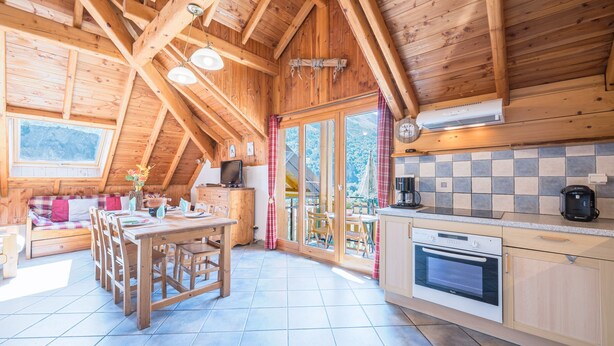 Un interior de madera con cocina, comedor y un amplio ventanal con vistas a un paisaje montañoso.