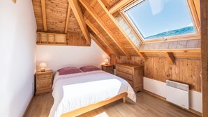 Un dormitorio con techo de madera inclinado, tragaluz, cama, mesitas de noche y un calentador.