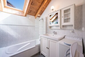 Une salle de bain moderne dotée d’un puits de lumière, d’une baignoire sur pieds, d’un lavabo intégré et d’un lave-linge.