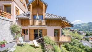 Un chalet de madera de dos plantas con balcón, un patio amoblado y vistas del paisaje circundante.