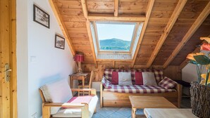 Acogedor dormitorio en ático con techo de madera, tragaluz, cama, sofá y una pequeña mesa.