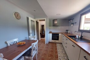 A kitchen with a wooden table, white chairs, a clock, and a window.